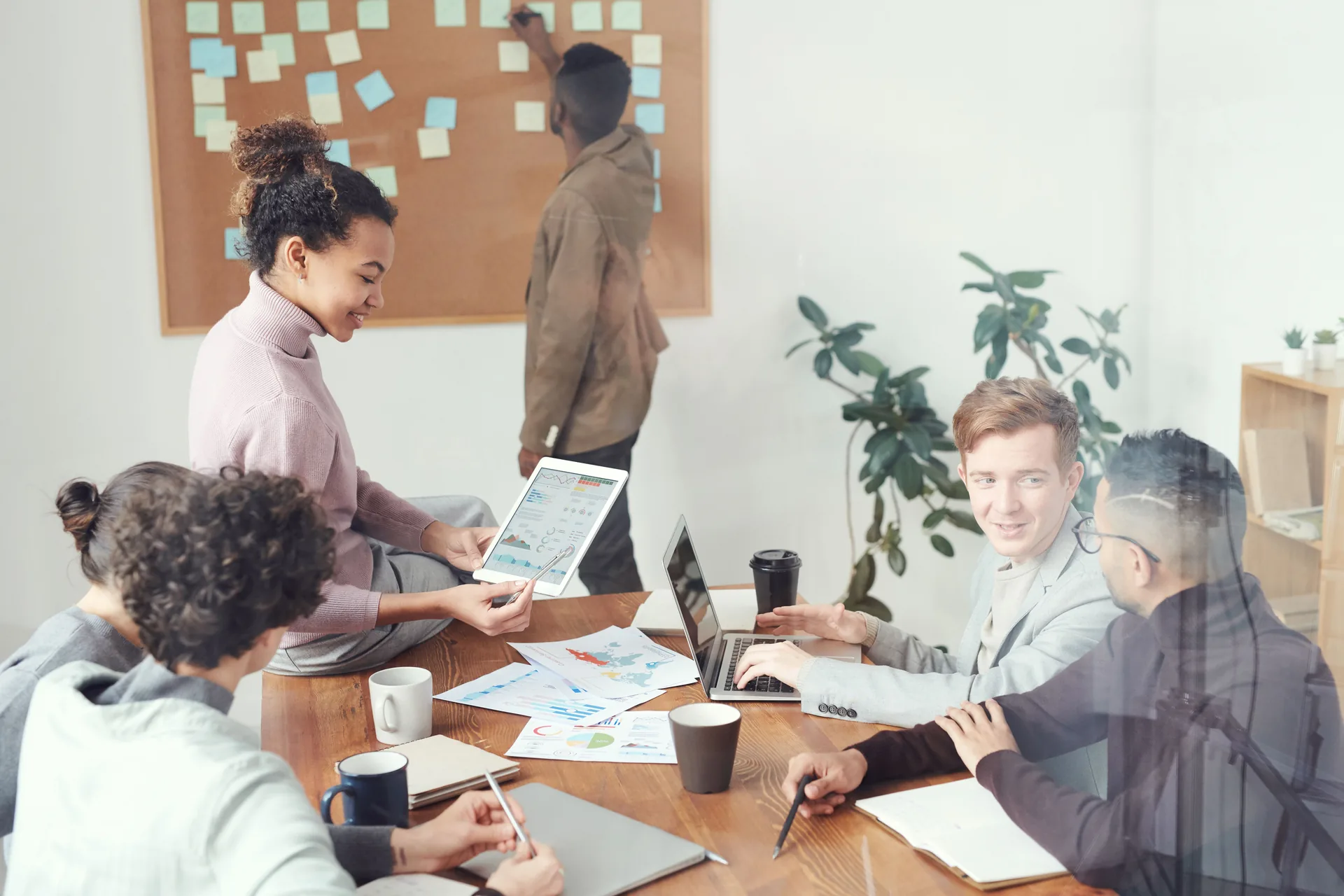 Koordinatorin steuert am Planungsboard ein Team am Besprechungstisch mit Laptop und Auswertungen